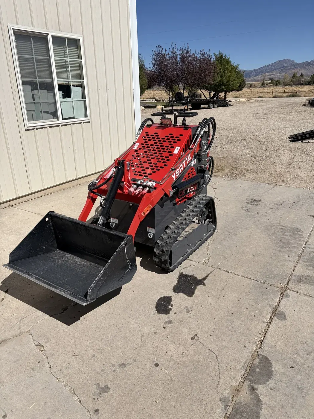 Weekend Warriors red mini ride-on skid steer with a tracked undercarriage and front bucket.